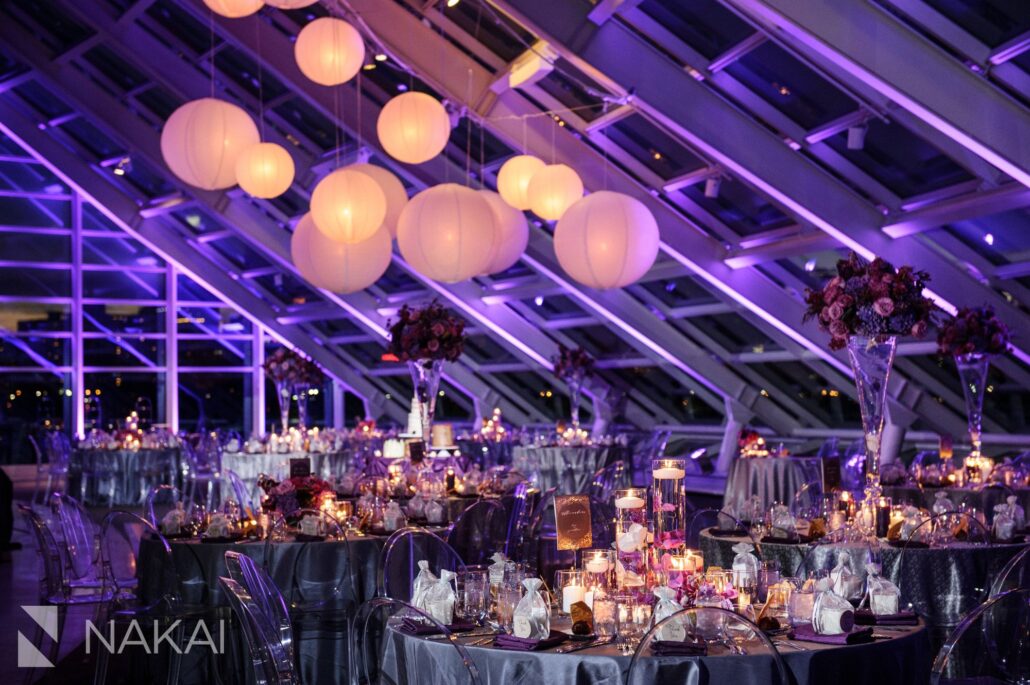 Elegant indoor event space with round tables set for dinner, floral centerpieces, hanging globe lights, and purple ambient lighting—perfect for couples seeking standout Greater Chicago Wedding Venues.