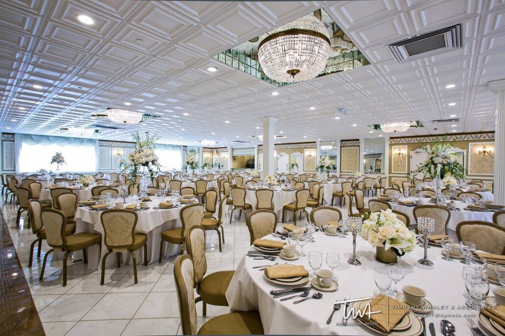 A large, elegant banquet hall—one of the top Greater Chicago Wedding Venues—is set up for an event with round tables, beige chairs, floral centerpieces, chandeliers, and polished white floors.