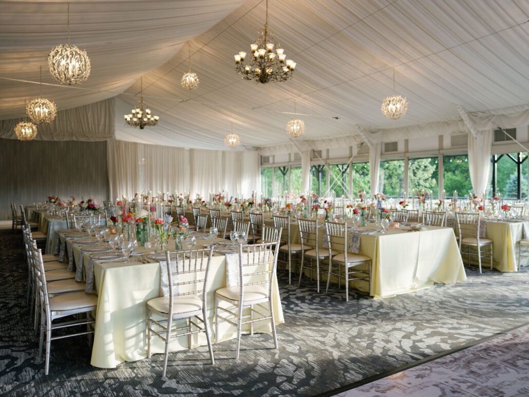 A large banquet hall with rows of tables covered in light yellow tablecloths, set with glassware and floral centerpieces, under chandeliers and globe lights—perfect for those seeking Greater Chicago Wedding Venues.