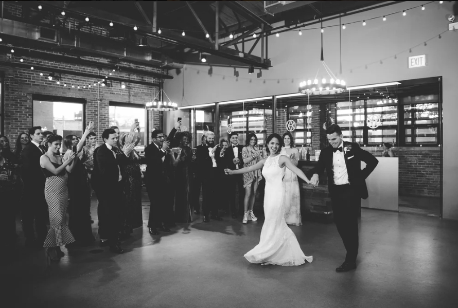 A bride and groom dance together in the center of a spacious, industrial-style venue as guests watch and take photos—an unforgettable moment at one of the top Greater Chicago Wedding Venues.