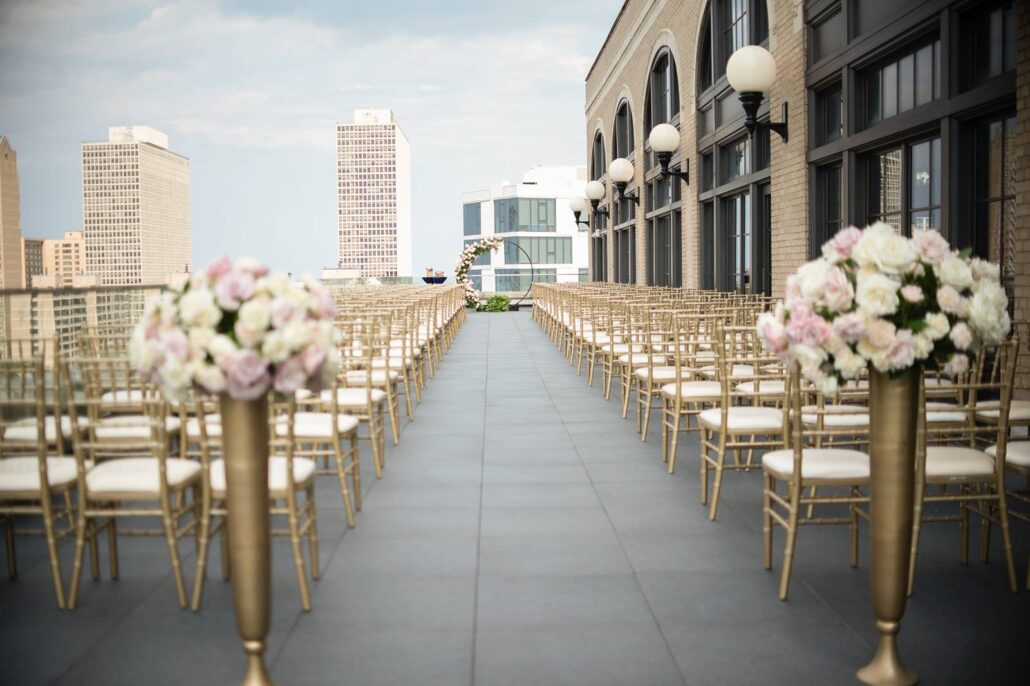 Outdoor rooftop wedding venue with rows of gold chairs, flower arrangements, and a city skyline in the background—one of the standout Greater Chicago Wedding Venues for a memorable celebration.
